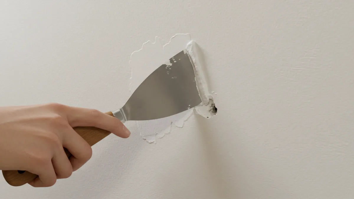 Mano con spatola che stucca un piccolo foro su una parete interna